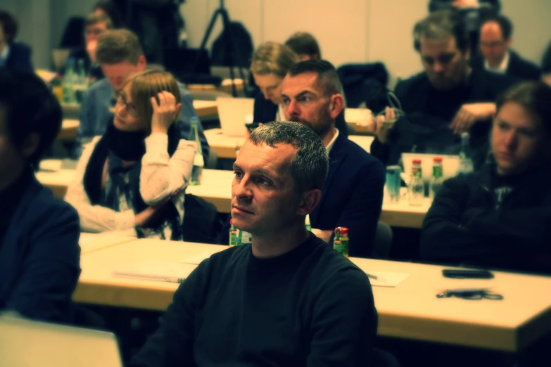 people seated in a conference room, watching other people