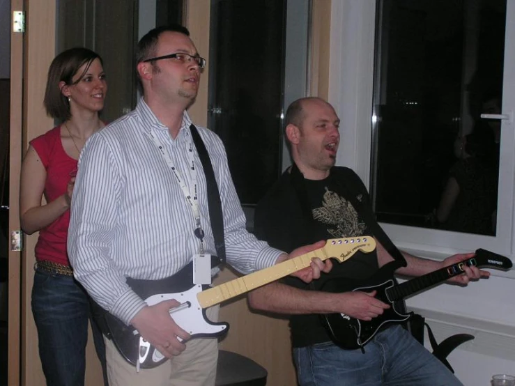 two people standing in front of a window one playing an electric guitar and the other holding a black guitar