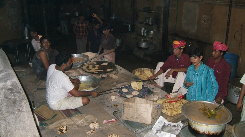 several people cooking and standing around a table full of food