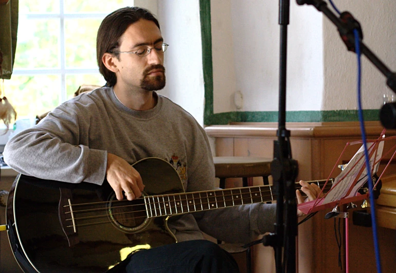 a man with glasses playing an acoustic guitar