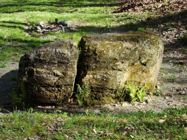 a large rock in the middle of an area with some green grass