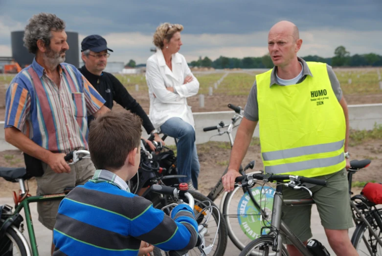 three people in safety vests, one of which is talking to a man with several bikes