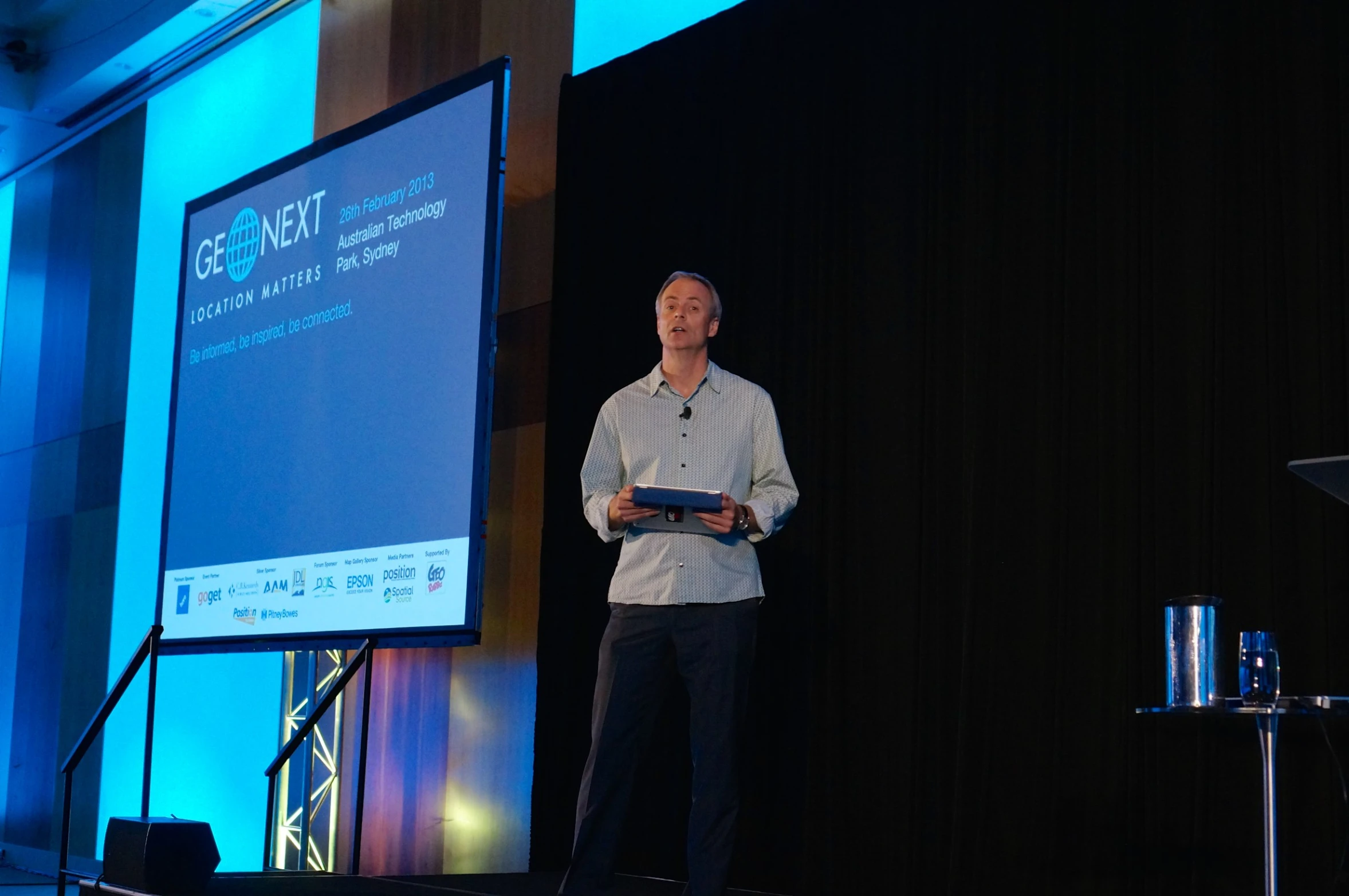 man with a tablet standing on stage at conference