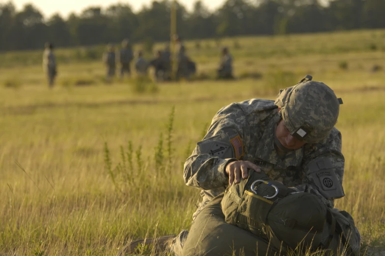 a soldier sitting in a field with an object in his hand