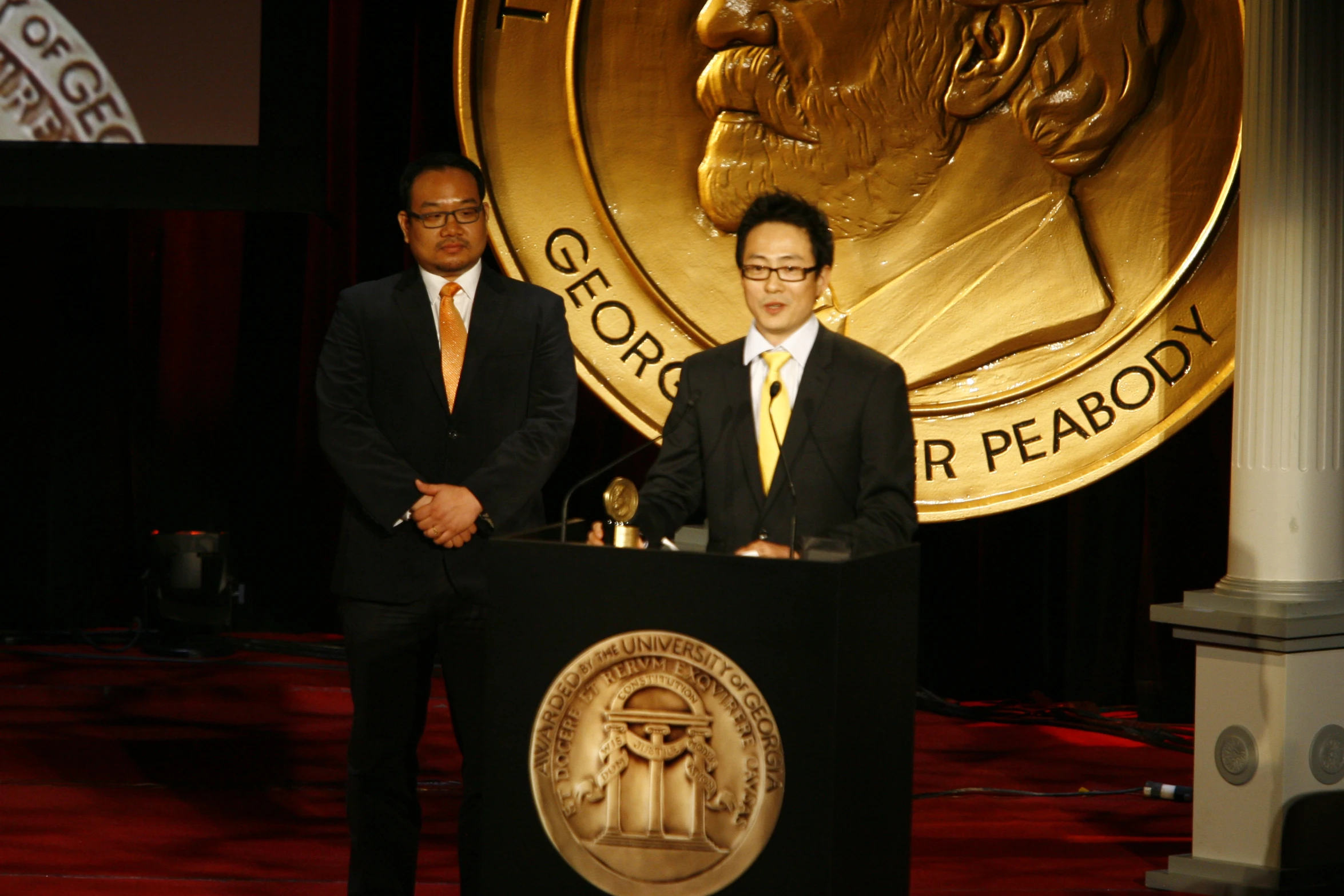 two men standing behind the podium in front of the logo