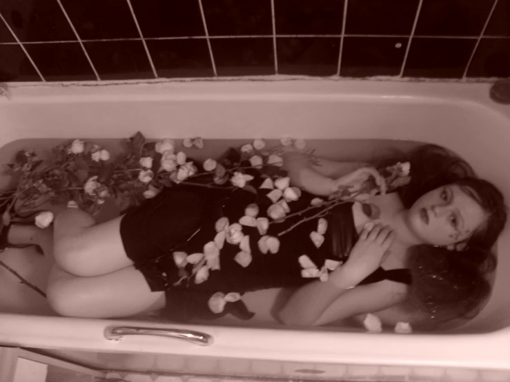 a woman lays down in a bathtub surrounded by white flowers