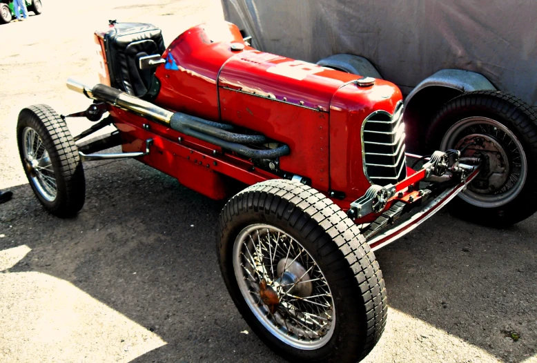 an old, red car sits on a lot next to a tent