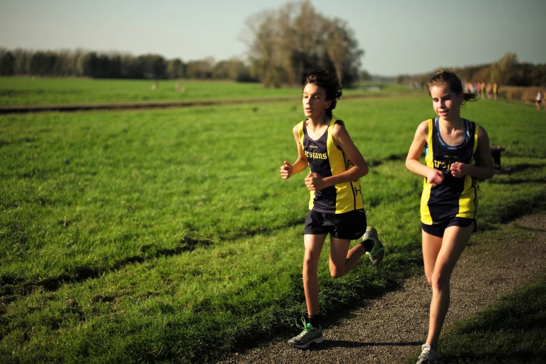 two boys are jogging on the grass near the road