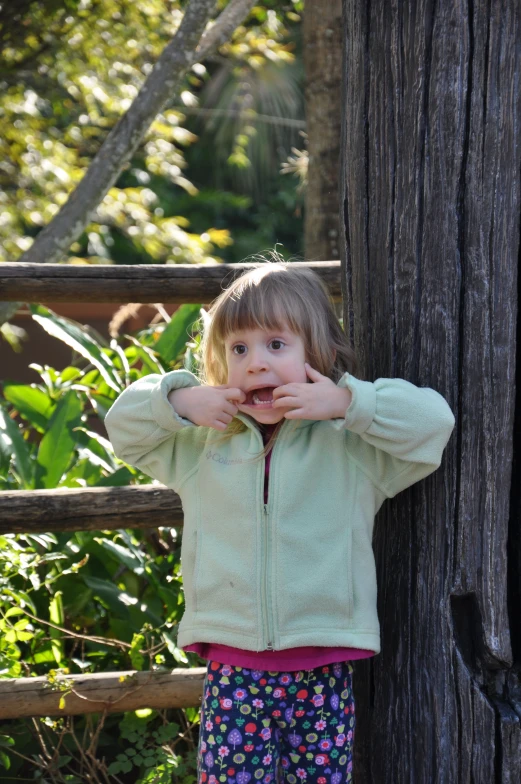 a little girl in blue is holding her hands on the side of a wooden wall