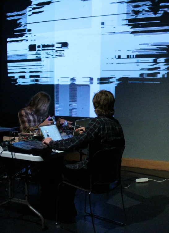 two people sitting at a desk in front of a monitor