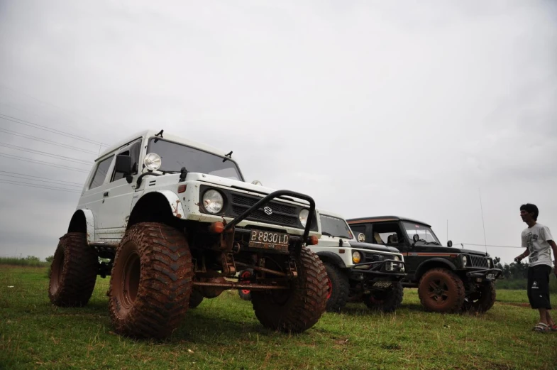 several jeeps are parked in the field behind large tires