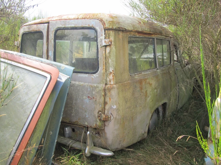 an old bus that is rusted sitting in the weeds