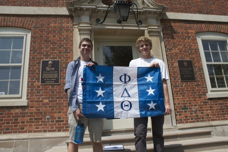 two men holding a banner standing in front of an old building