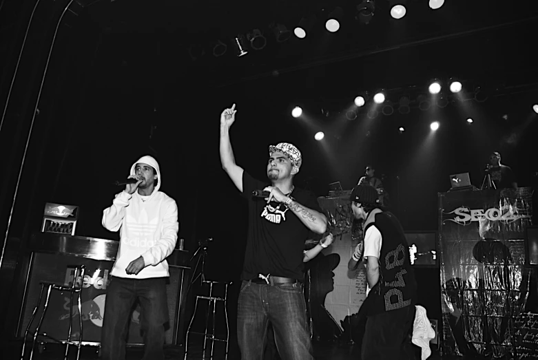 three men standing on stage at night with their arms in the air