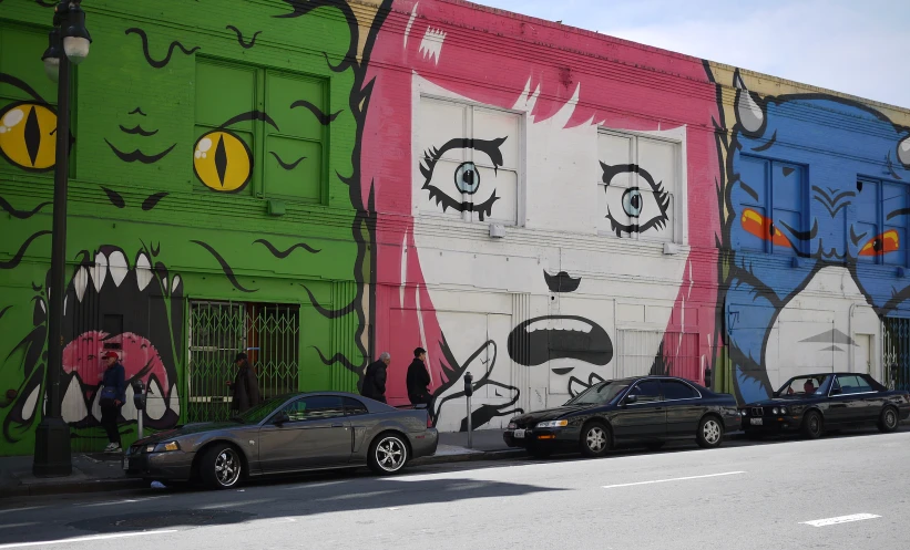 cars are parked on the side of a building painted with images