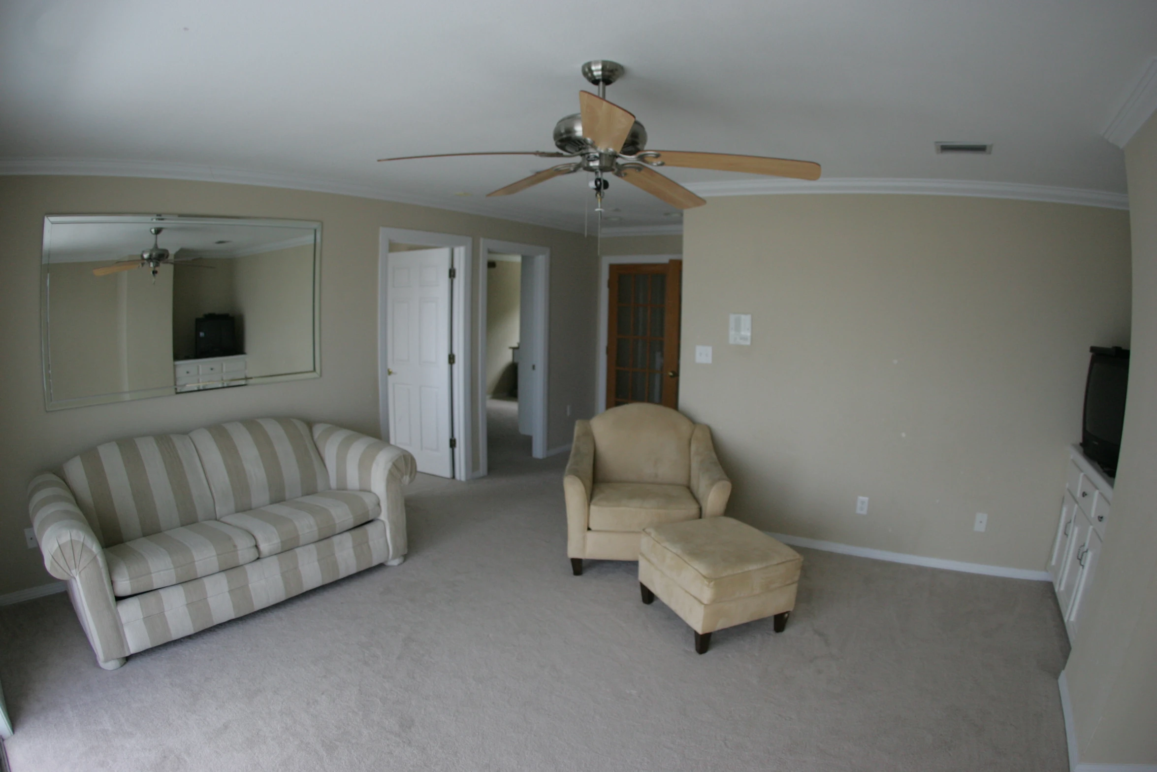 a light beige living room with a fan, chair and ottoman