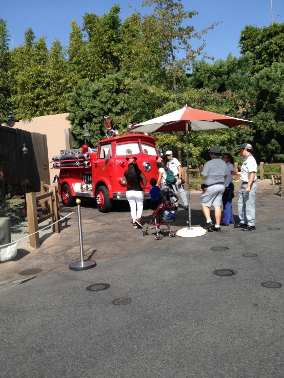 a group of people are gathered around the red car