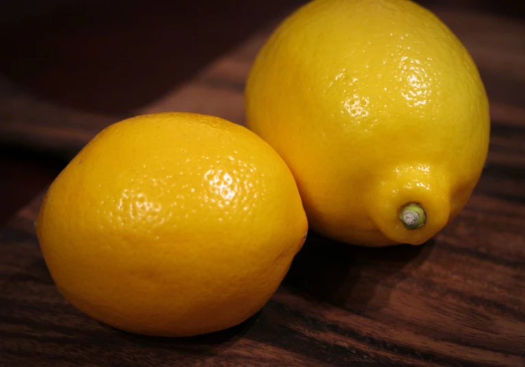 two lemons sitting on a wooden surface next to each other