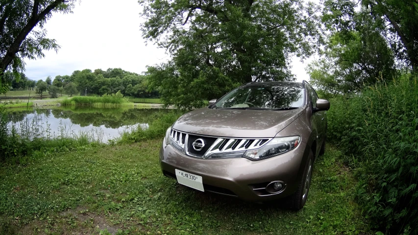 the silver car is parked in the grass by a pond