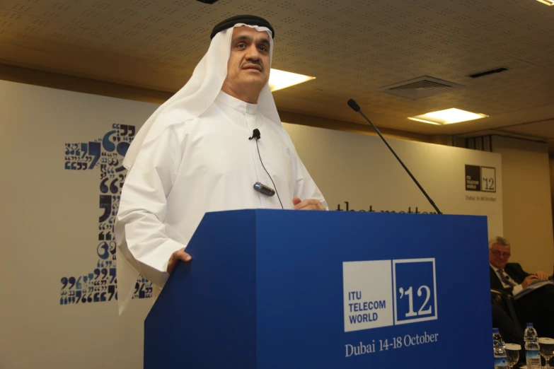 a man in white shirt and headdress speaking into microphone