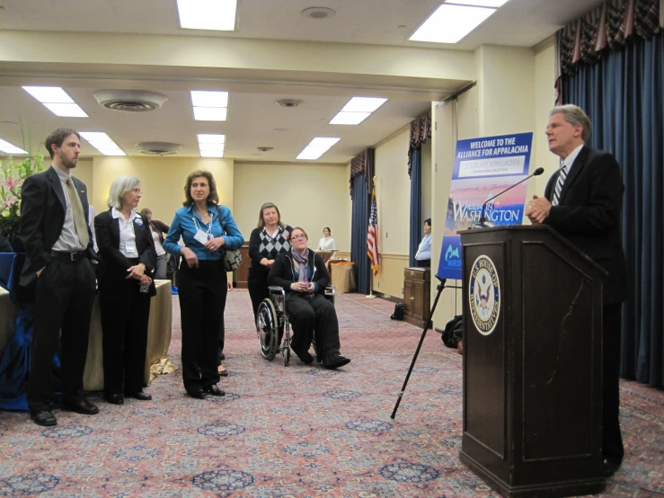 a group of people in a room, one of them is speaking at a podium