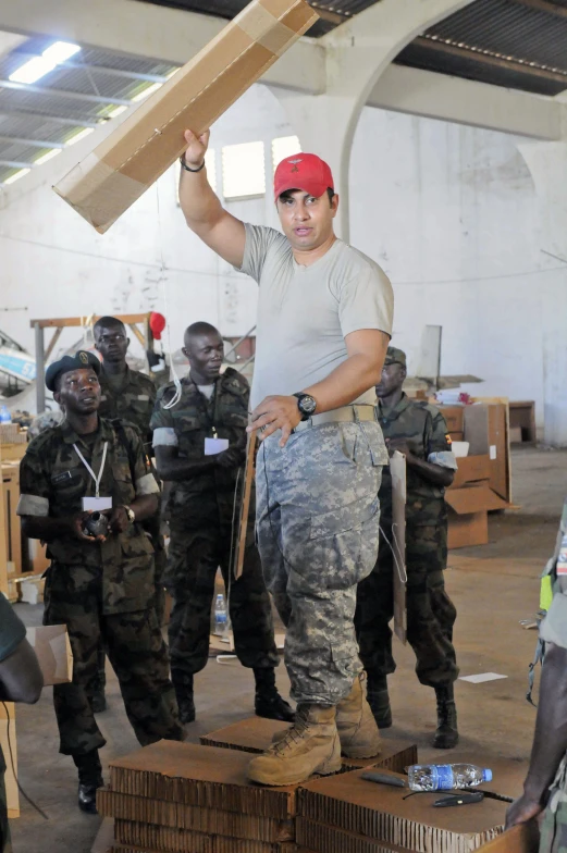 a man wearing a red cap is holding a large wooden item in front of a group of men