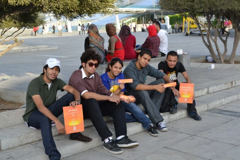 six people are holding orange books while they sit on a set of stairs