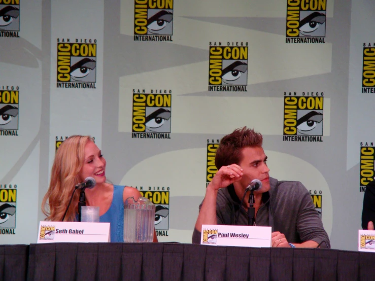 actors sitting at a panel with comic characters behind them