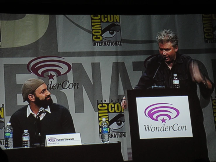 two men are speaking at a panel of paneled comic