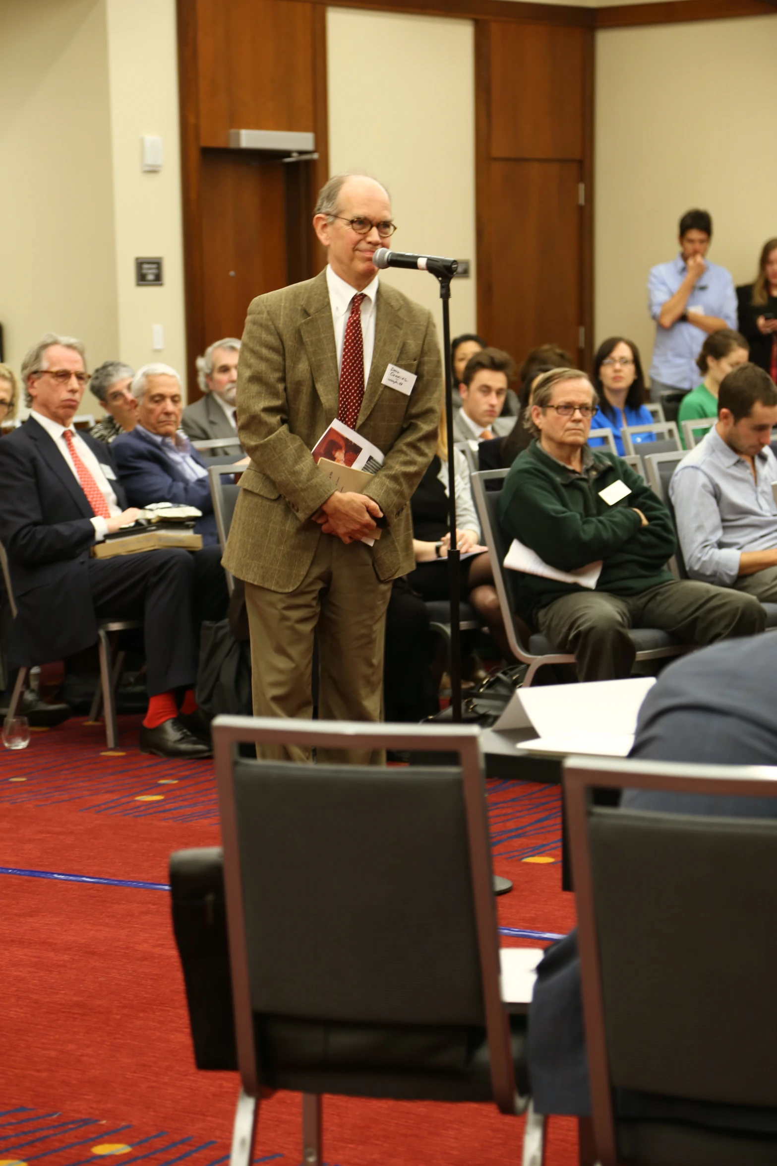 man in business attire on stage with audience behind him