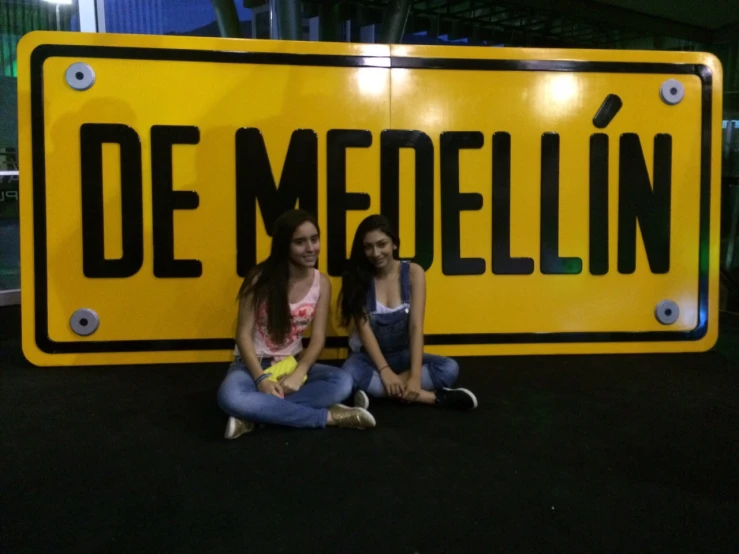 two young ladies are sitting under a sign