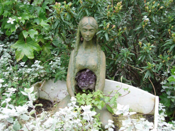 a stone statue in the garden with water coming out of it