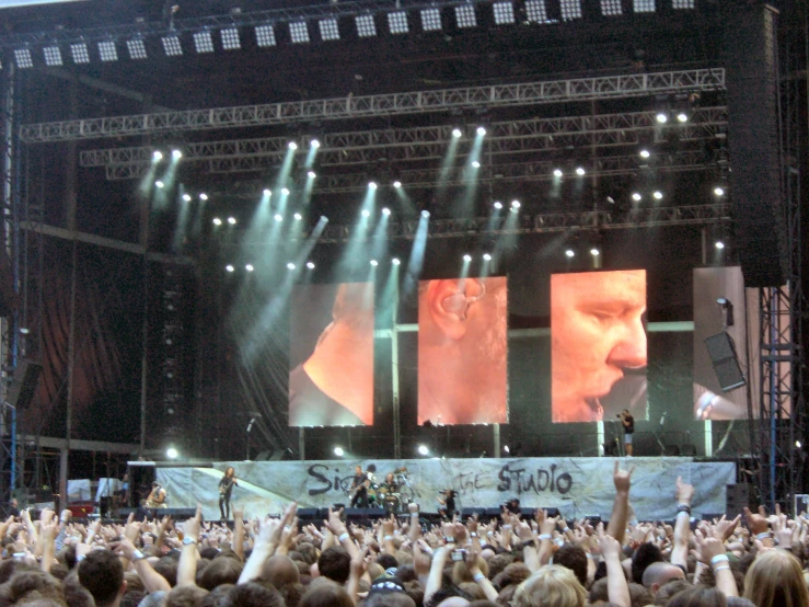 crowd of people with cell phones up to their ears as they watch a concert on a big screen