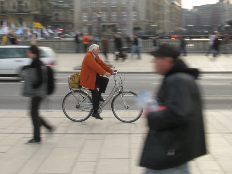 a man in a orange jacket rides on a bicycle with a basket