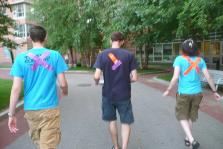 three boys with blue shirts are walking down a sidewalk