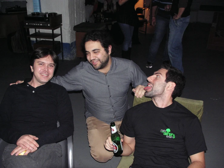 three men sitting next to each other with one drinking beer