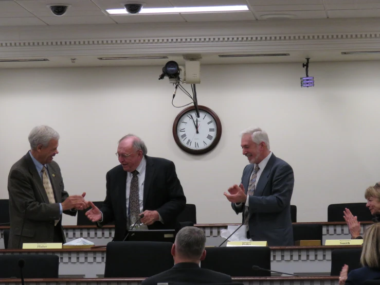 three men in suits talk with two other men in front of a table in a courtroom