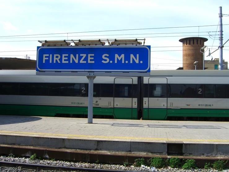 a white and green train traveling past a tall blue sign