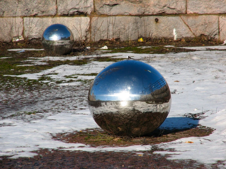 two shiny balls stand in the mud on an outdoor lot