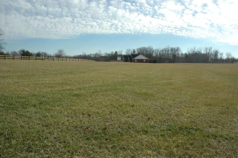 a field with fence around it and a house in the distance