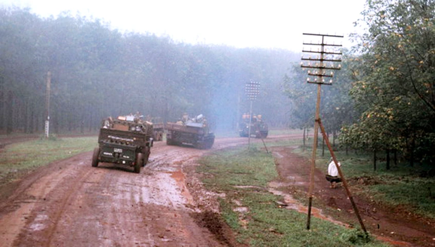 a row of vehicles driving on a dirty dirt road