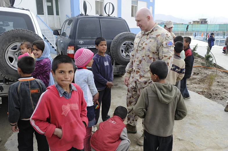 military man talking to s in front of a car