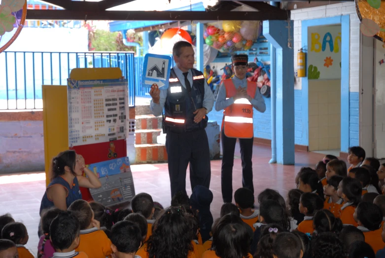 a man wearing an orange vest giving a speech in front of children