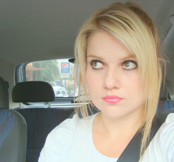 a blond woman in a white shirt is driving a car