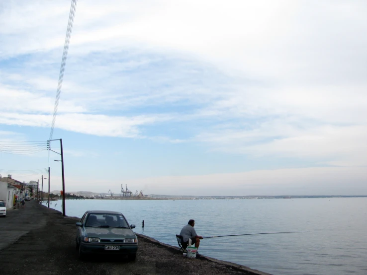 a man fishing while his car is parked near him