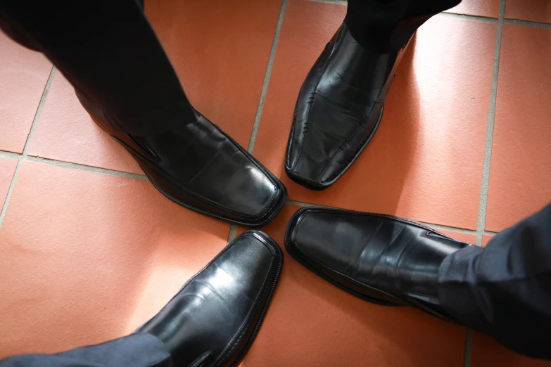 four men's legs and one is standing in black dress shoes