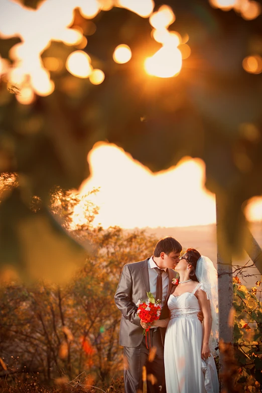 a bride and groom standing in front of a sunset