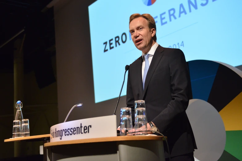 a man at a podium speaking into two empty bottles