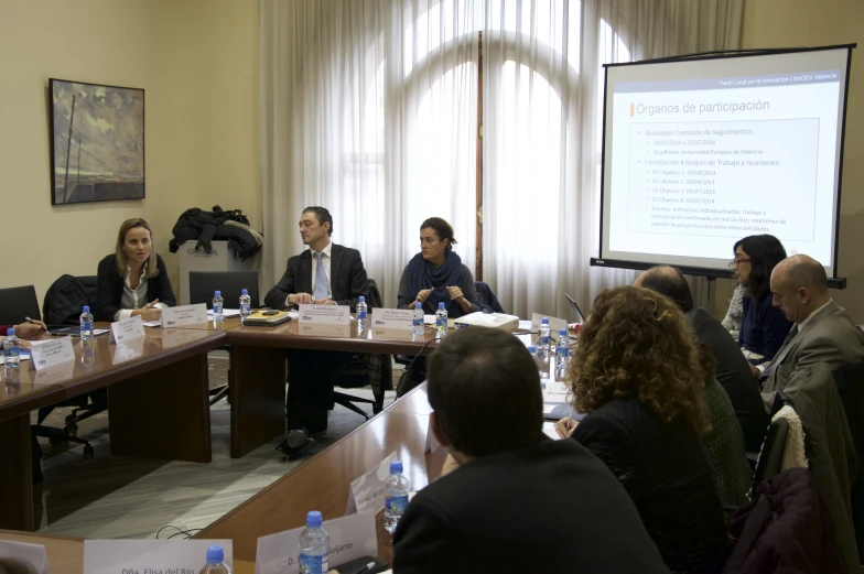 a group of people at a meeting, sitting around a wooden table