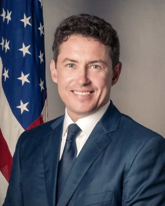 a well dressed businessman smiles in front of an american flag